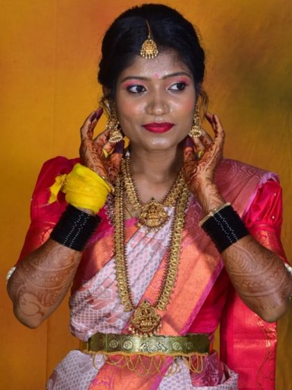 A traditional bridal portrait. This bride is adorned in classic temple jewelry, a bright red lip, and makeup that accentuates her features against a vibrant studio backdrop.