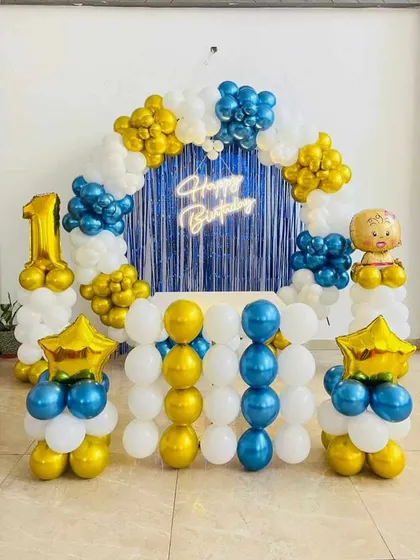 A complete birthday party setup perfect for your home. This decoration includes a balloon arch, a 'Happy Birthday' neon sign against a shimmer curtain, a light-up number '1', and balloon pillars with a cute baby foil balloon on top.