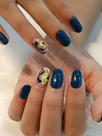 A stylish manicure with a mix of solid navy blue and abstract yellow and black art on the accent nails.