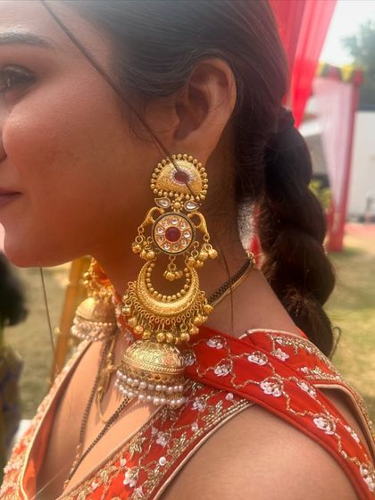 A client wearing a pair of multi-tiered gold jhumkas with red stone accents, paired with a red saree. This shows how my jewellery can be styled for real events.