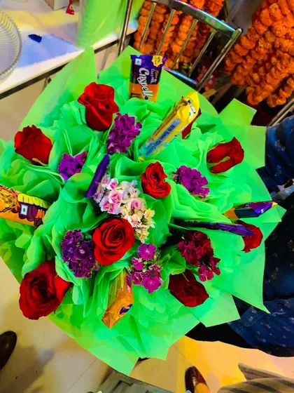 A vibrant and colorful custom bouquet. This arrangement features red roses and purple statice mixed with various chocolates, all wrapped in bright green paper for a fun and eye-catching look.