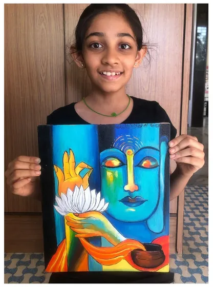 A student proudly displays her stunning canvas painting of Buddha, featuring a vibrant blue and green palette and a beautifully rendered lotus flower.