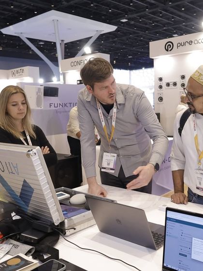 An exhibitor provides a detailed walkthrough of their system's software on a laptop to a potential client and partner, showcasing the backend technology.