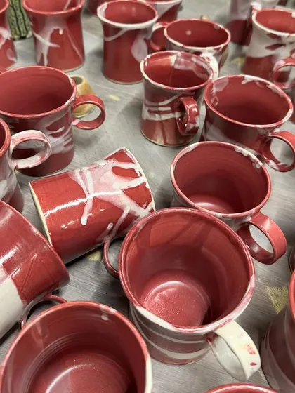 A table full of freshly glazed mugs from our Flamingo series. The swirling patterns of red and white are different on every single piece.