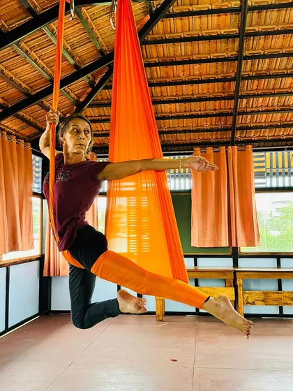 A student demonstrates a graceful pose in the orange aerial hammock, showcasing the strength and flexibility gained during our TTC.