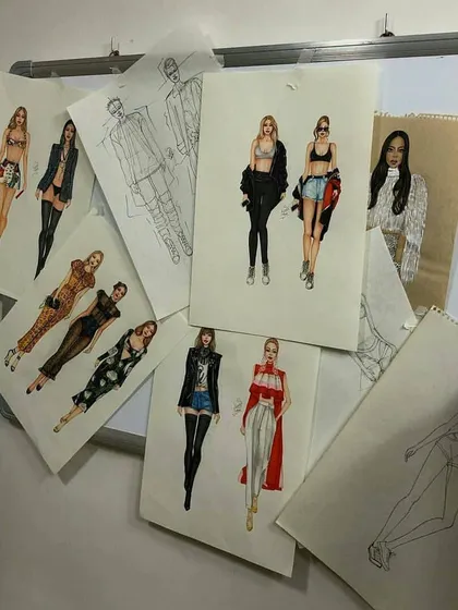 A display of student fashion illustrations on a whiteboard. This collection includes both rough pencil sketches and fully colored designs, showing the progression of an idea from a simple concept to a finished presentation piece.