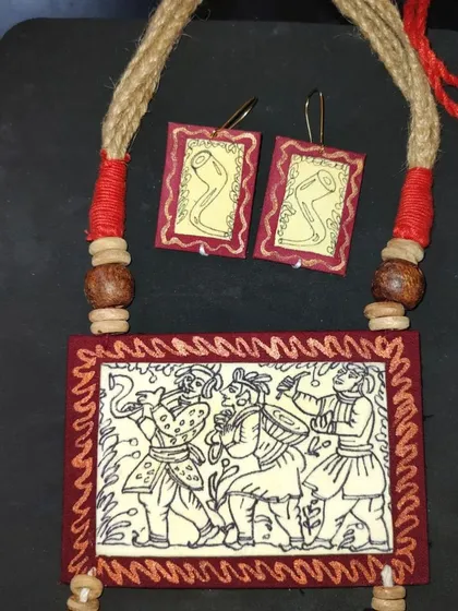 This image shows the Jamini Roy inspired necklace set on a dark surface, highlighting the detailed line work of the painted figures on the fabric pendant.