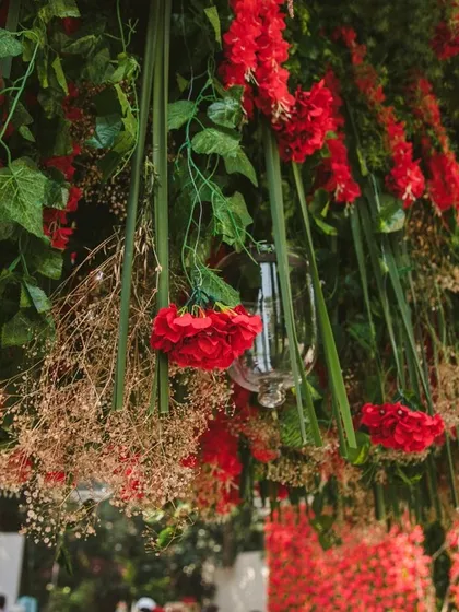A close-up of the hanging red wisteria, showing the intricate layering of different textures and shades. The inclusion of delicate baby's breath and varied greenery adds depth and a natural feel to this bold floral statement piece.