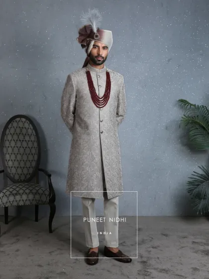 Crafted for the modern prince, this coffee beige sherwani in jacquard and aari detailing is an ode to Indian heritage. The two-tone turban and ruby mala add a personalized, regal touch.