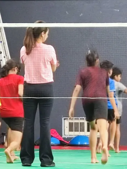 Observing and guiding young athletes during their warm-up drills on the badminton court. Proper warm-ups are essential for preparing the body for intense activity.