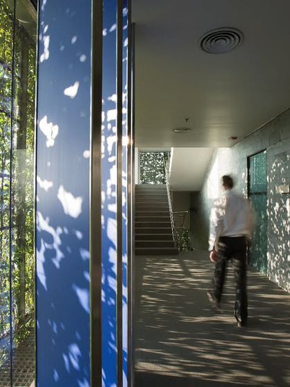 The interplay of light and shadow through the green facade creates a dynamic interior environment at the KMC Headquarters. This corridor view shows how the building's skin filters sunlight, creating a serene and constantly changing atmosphere.
