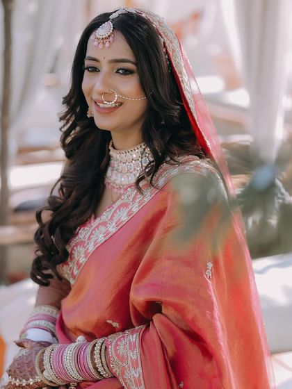 A smiling portrait of a bride in her pink wedding saree, captured in bright, natural light.