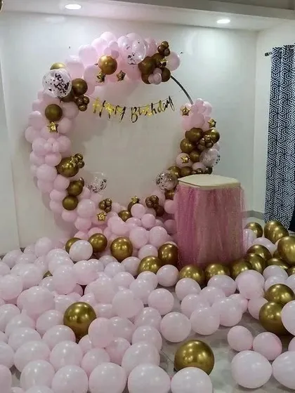 A room filled with pink and gold balloons for a birthday surprise, featuring a circular balloon arch and a cake table.