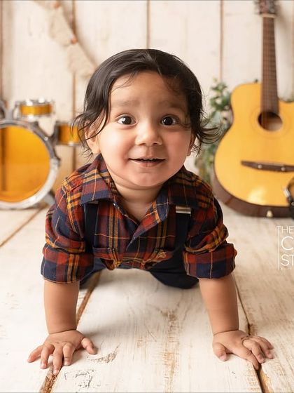A future rockstar on the move. This little boy crawls towards the camera with a huge smile, with a mini drum set and guitar in the background.