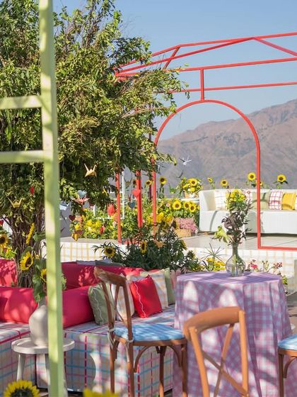 A red metal-frame structure creates a modern, open-air 'room' with a view of the mountains, filled with sunflowers.