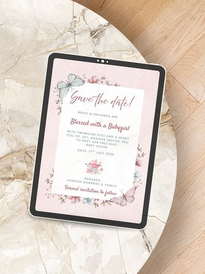 A sweet and delicate Save the Date for a baby girl's arrival. Displayed on a tablet, this digital design uses soft pinks, watercolor butterflies, and florals to announce the magical news.