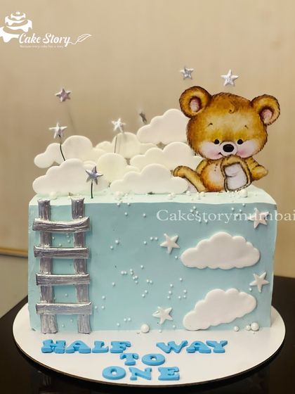 A 'Halfway to One' cake to celebrate a six-month milestone. This square cake features a cute teddy peeking out from behind fondant clouds and a ladder to the stars.
