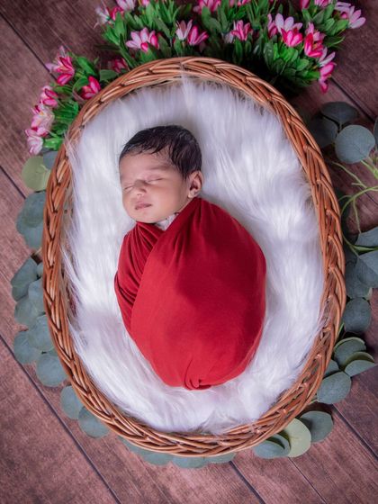 A perfect little rosebud. The bold red wrap contrasts beautifully with the soft pink flowers and rustic wooden background in this classic newborn portrait.