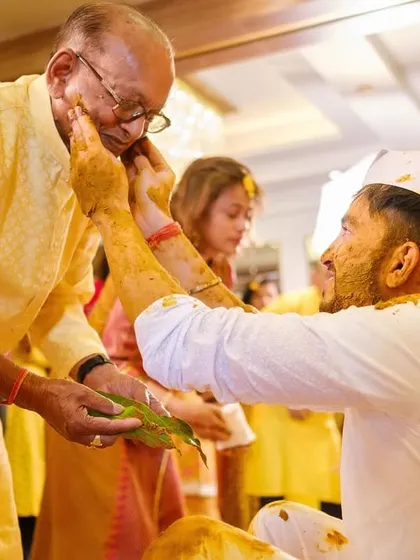 A touching moment of intergenerational respect and affection as the groom applies haldi to an elder's cheek.