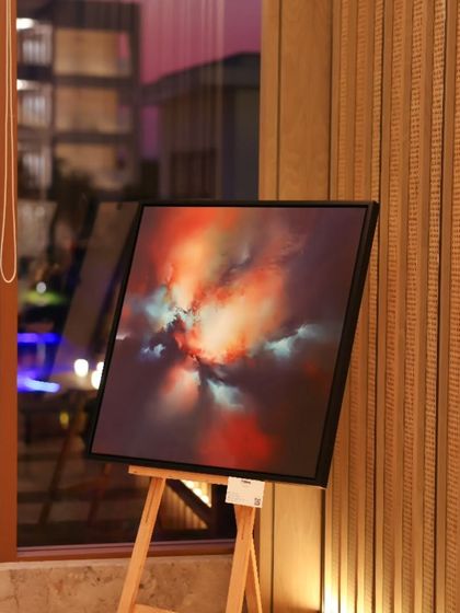 An abstract painting from the 'Mystic Mirage' show, set against the elegant wooden paneling of the JW Marriott. The setting enhances the artwork's dramatic, celestial feel.