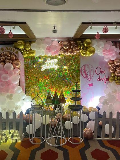 A glamorous first birthday with a gold shimmer wall, a pink and white balloon arch, and a cute picket fence detail.
