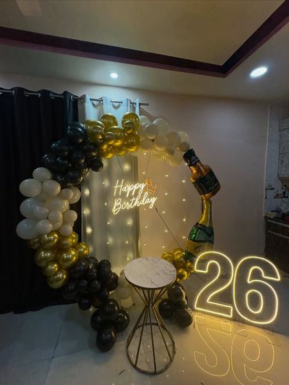 We designed this fun and stylish setup for a 26th birthday. The black, white, and gold balloon ring was accented with a whiskey bottle foil balloon and a light-up number '26', making it a perfect surprise for a husband's birthday.