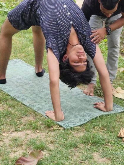 A young yogi explores his flexibility with a wheel pose in the park, getting hands-on assistance to ensure he practices the pose safely.