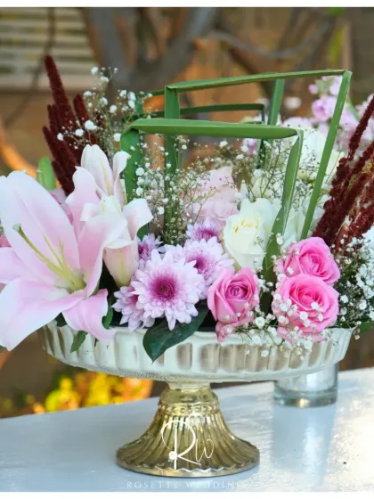 A beautiful floral arrangement in a gold-footed bowl, combining pink lilies, roses, and chrysanthemums for a rich and textured look.