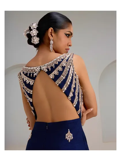 The back of this navy blue jumpsuit reveals its dramatic elegance. The open-back design is framed by intricate, cascading embroidery, making every turn a statement.