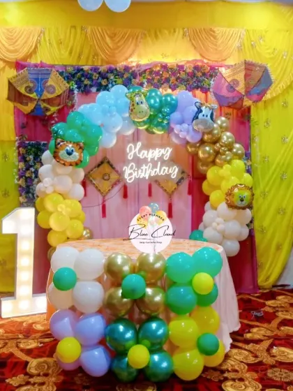 A colorful first birthday setup with a jungle animal theme. This decoration features a balloon arch with animal foil balloons, a neon sign, and a decorated cake table.