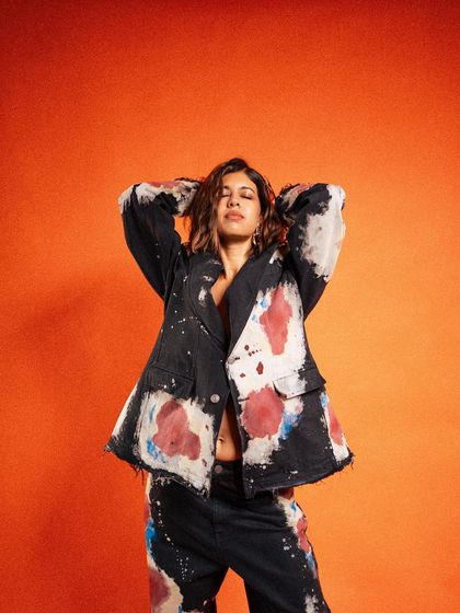 A relaxed and cool pose, with hands behind the head. This shot exudes confidence and showcases the unique, paint-splatter design of the jacket in a natural, effortless way.