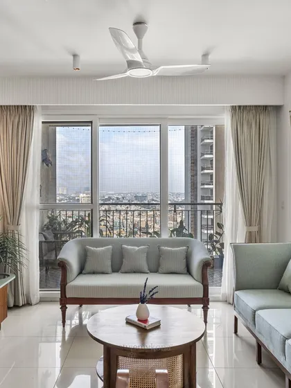 A serene view of the living room, with the sofa perfectly positioned to enjoy the city view through the large glass doors. The neutral curtains and light-colored furniture enhance the feeling of openness and tranquility.