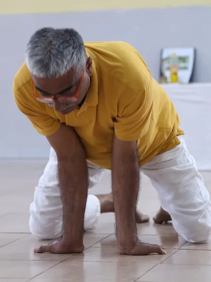 A teacher prepares for Mayurasana, the peacock pose, demonstrating the initial steps to build strength in the wrists and forearms.
