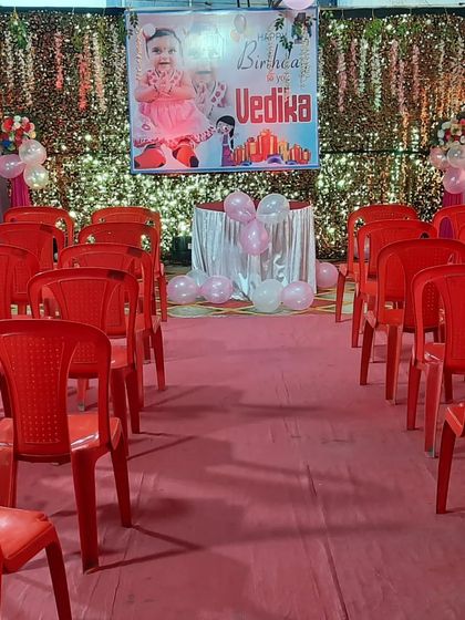 A full view of the birthday setup for Vedika, showing the stage, backdrop, and seating arrangement with red chairs.