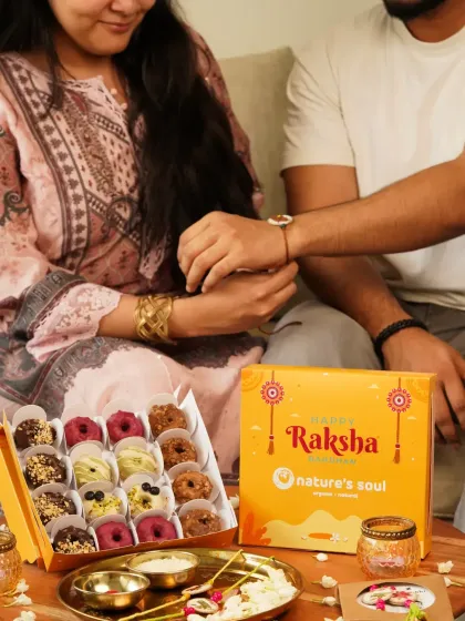 A heartwarming moment of a sister tying a rakhi on her brother's wrist during Raksha Bandhan, with a box of festive doughnuts ready to be shared.