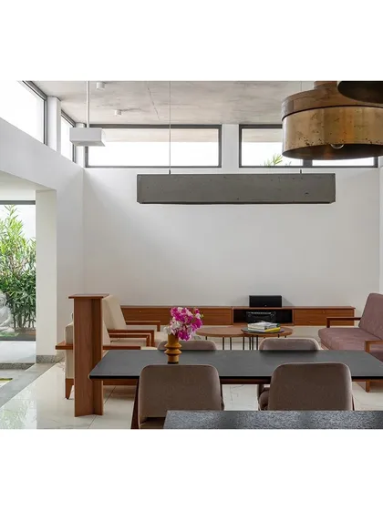 The double-height living and dining area in the SAMAM House, demonstrating our use of volume to create a sense of spaciousness. Large windows frame views of an outdoor courtyard and a tranquil Buddha statue, integrating calm and nature into the main living space.