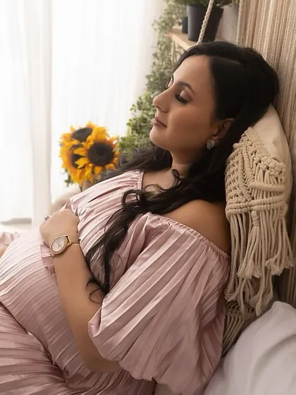 A peaceful and serene moment captured in my studio's cozy corner. The mom-to-be is resting against a pillow, eyes closed, gently holding her bump in a beautiful off-the-shoulder pink dress.