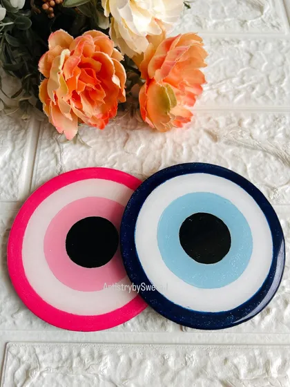 A pair of my handcrafted evil eye coasters, one in pink and one in blue. They are perfect for adding a touch of protective style to your coffee table.