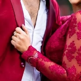 A detail shot that speaks volumes. The intricate lace on the sleeve of the red gown against the partner's matching jacket highlights the coordinated styling available for couples.