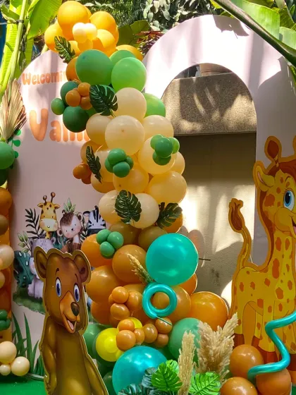 A wild welcome for baby Vamika. This jungle-themed setup features a large balloon arch in earthy greens, oranges, and yellows, complete with cute bear and giraffe cutouts, creating an adorable safari adventure.