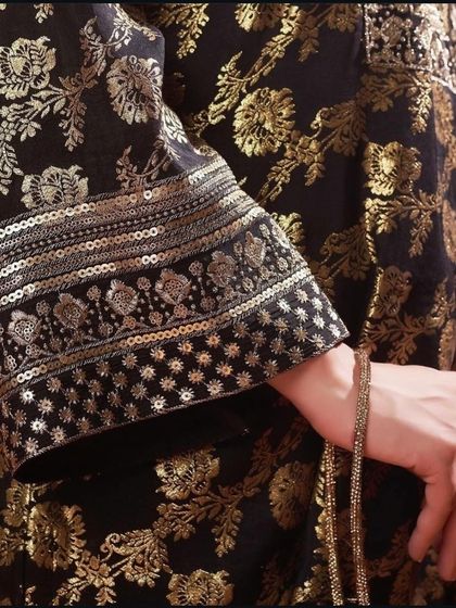 A close-up of a black Banarasi brocade sleeve, showing the rich texture of the gold weaving and the sequined cuff.