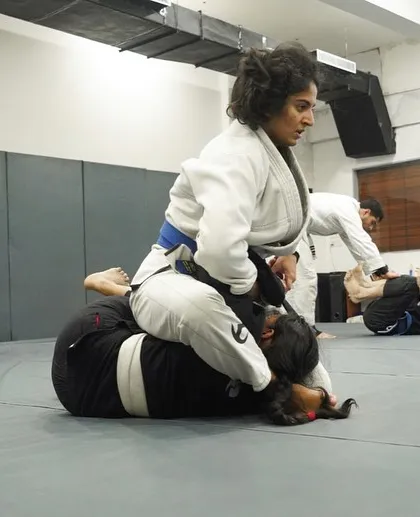 A female student in a white Gi practices maintaining the mount position. We emphasize live drilling to ensure our students can apply what they learn.