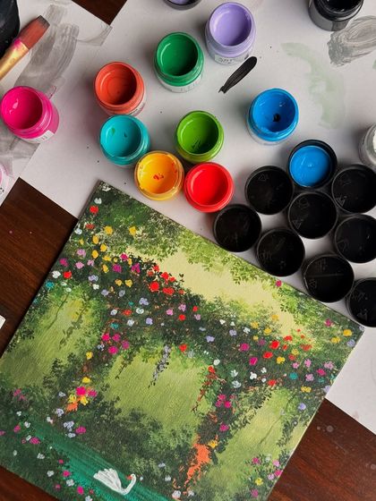 A flat-lay of the swan lake painting surrounded by some of the many acrylic paint colors I used to create it. It shows the vibrant palette behind the magic.