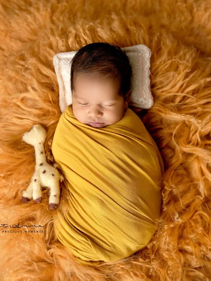 A burst of sunshine. This baby is wrapped in a vibrant yellow swaddle on a fluffy orange blanket, creating a warm and cheerful portrait.