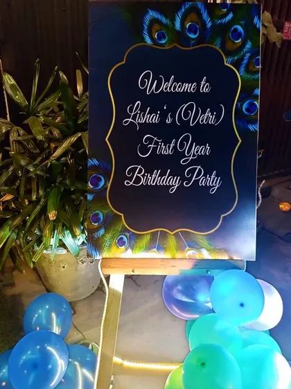 A custom welcome board for a peacock-themed first birthday party. Placed on a wooden easel and surrounded by balloons, this sign warmly greets guests and introduces the event's beautiful theme.
