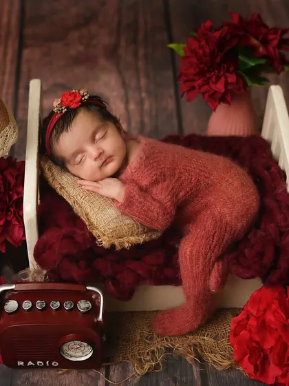 The full 'vintage romance' setup, with the baby sleeping in a miniature bed surrounded by red flowers and a retro radio.