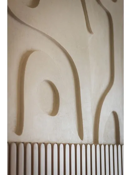 A close-up of the custom Art Deco wall paneling behind the bed. The organic, carved shapes create a beautiful play of light and shadow, adding a layer of artistry to the space.