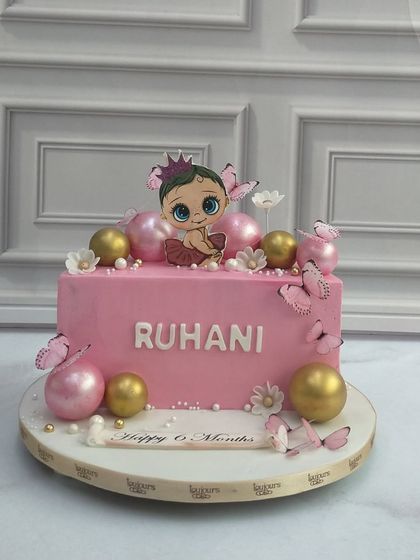 Celebrating a sweet milestone with this rectangular pink cake for a six-month birthday. It's decorated with pretty butterflies and pink and gold spheres, personalized with the baby's name.