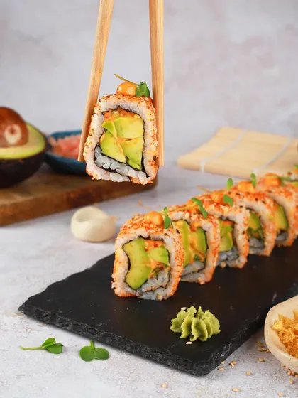 The perfect bite of an avocado sushi roll, held up by chopsticks. This shot is all about that fresh, creamy texture and is designed to be clean, modern, and super appetizing.