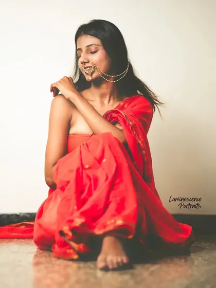 A seated portrait in a red saree, styled in a modern strapless fashion, capturing a moment of quiet contemplation.